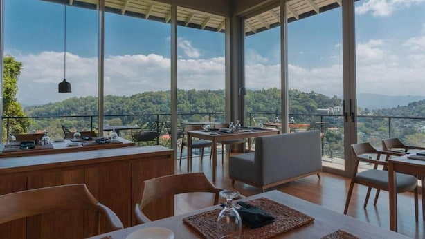 Un comedor con ventanas amplias, una mesa de madera y sillas.