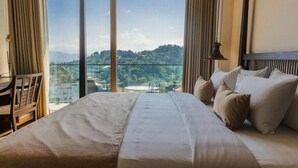 Habitación de hotel con una cama grande, un escritorio y vistas a un balcón con un paisaje pintoresco.