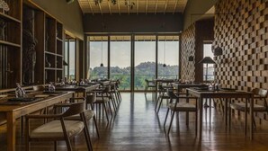 Un restaurante con mesas y sillas de madera, ventanas amplias con vistas a las colinas y un patrón de pared a cuadros.