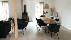 A modern living room with a wooden dining table, black chairs, a sofa, and a black fireplace. - Holiday Home 'Strand Haus' with Private Terrace, Private Garden and Wi-Fi (Elsfleth)