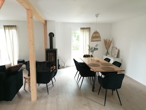 A modern living room with a wooden dining table, black chairs, a sofa, and a black fireplace.
