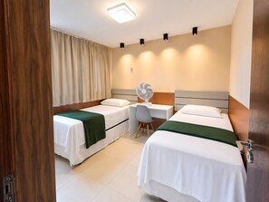 Ein Hotelzimmer mit zwei Betten, einem Schreibtisch, einem Stuhl, einem Ventilator und einer Tür.