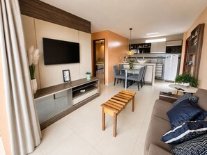 Un salon moderne dotĂ© dâun tĂ©lĂ©viseur Ă Ă©cran plat, dâun banc en bois, dâun canapĂ© agrĂ©mentĂ© de coussins Ă motifs et dâun coin repas avec des chaises et une table.