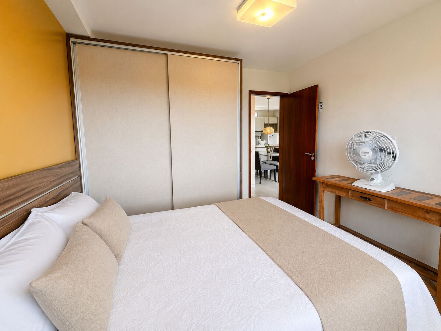 Et hotelværelse med en seng, et natbord med en ventilator, et klædeskab og en dør til et tekøkken.