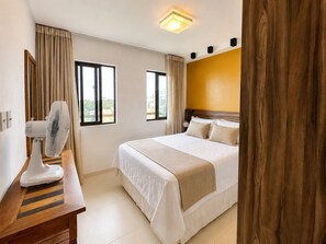 A hotel room with a bed, a desk with a fan, two windows, and a wooden headboard.