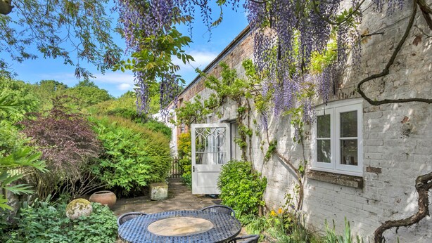 A garden with a table and chairs, a white door, and a brick wall. - Finest Retreats | The Pottage (Oakley)