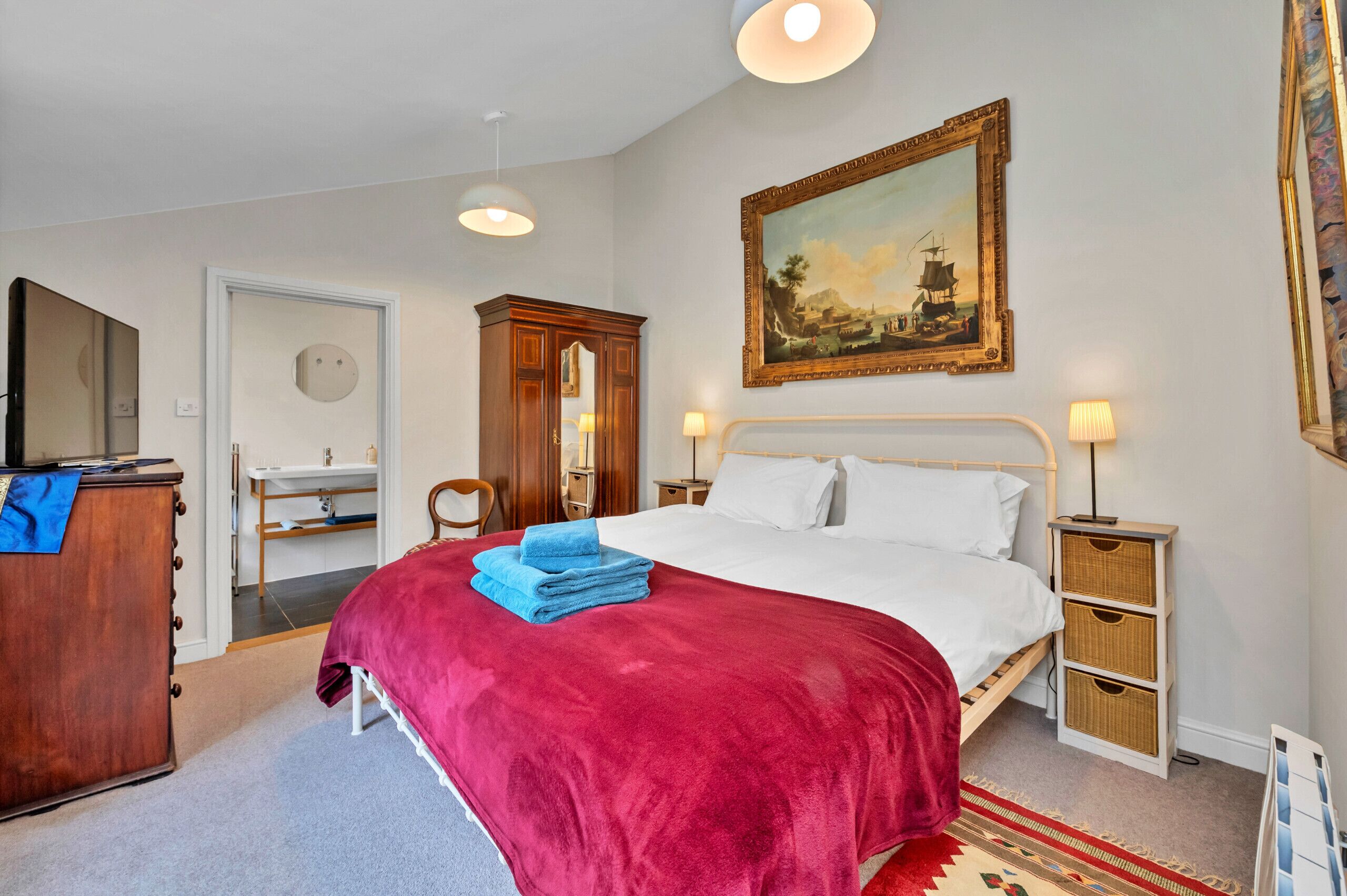 A bedroom with a bed, a dresser, a mirror, a nightstand, a lamp, and a painting on the wall.
