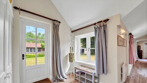 A hallway with a white door, a bench, and a window with curtains. - Finest Retreats | The Pottage (Oakley)