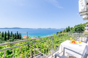 Ein Balkon mit gedecktem Tisch, mit Blick auf eine Küstenlandschaft mit Bäumen und Meer.