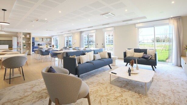 Un vaste espace de vie comprenant un grand canapé, une table basse et un coin repas avec des chaises et des tables.