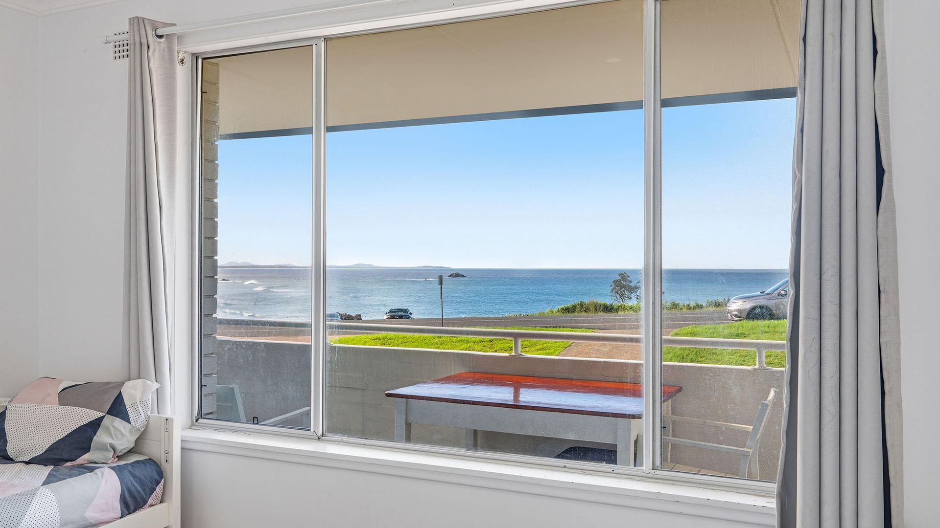 A room with a large window overlooking a coastal road with a view of the sea and a parked car.