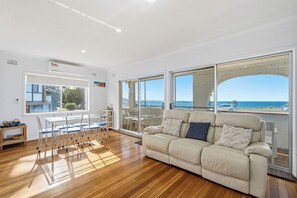 Ein Wohnzimmer mit Sofa, Esstisch, Stühlen und großen Fenstern mit Blick auf das Meer.