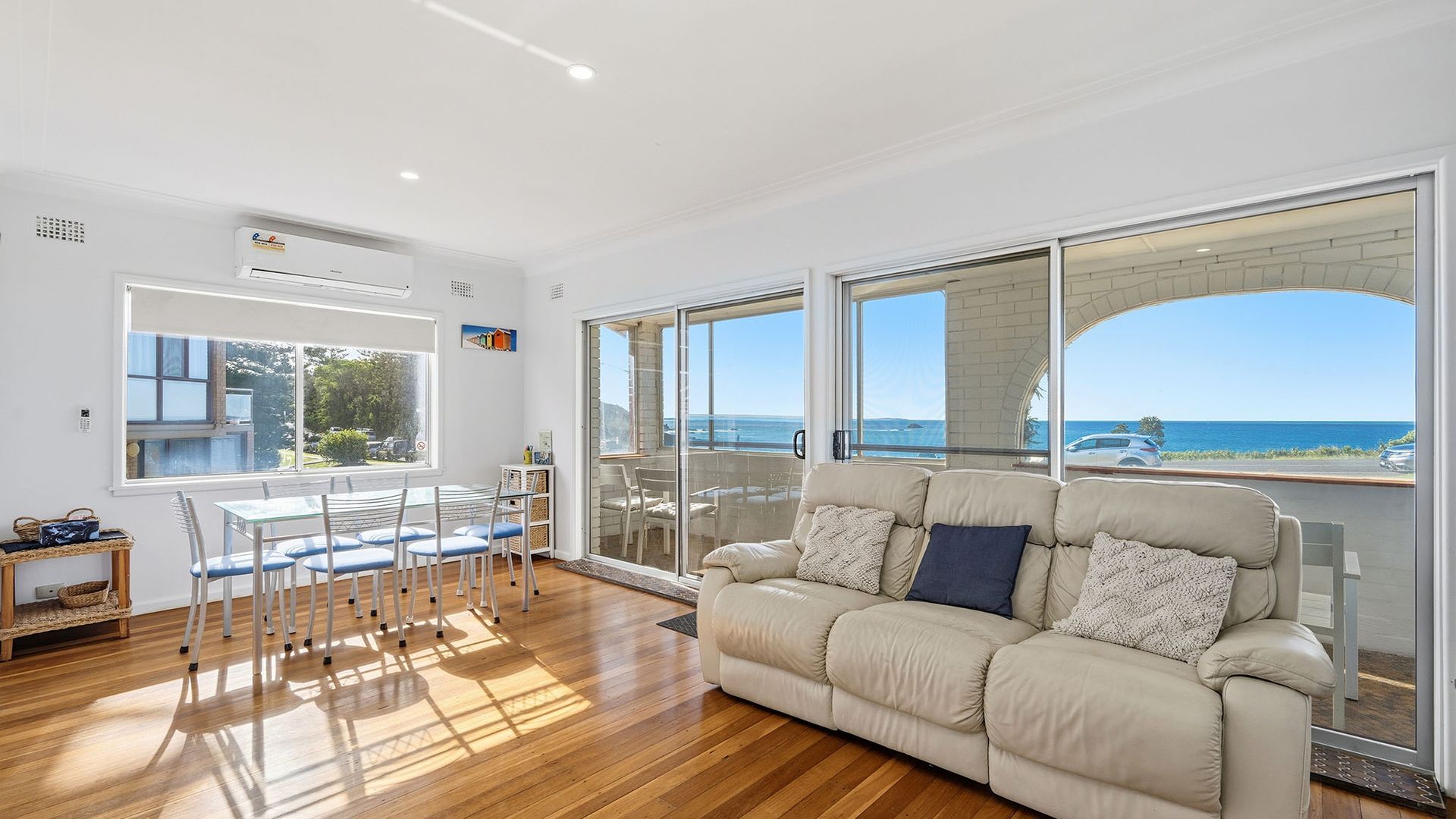 A spacious living area with a large window offering a view of the ocean, a beige sofa, and a dining table with chairs.
