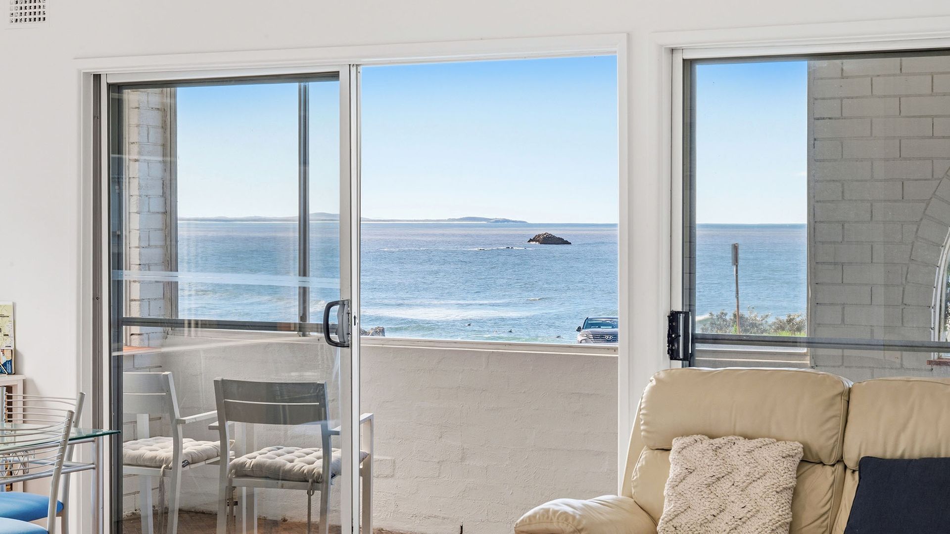 A room with a view of the sea, a glass door, a chair, and a sofa.
