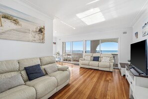 Ein geräumiges Wohnzimmer mit großem Fenster, einer Couch, einem Fernseher und einem Balkon mit Meerblick.