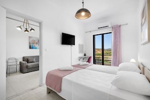 A hotel room with a bed, a TV, a desk, a chair, and a balcony with a view. - Sun Beach Apartment in Chania 14 (Chania)