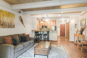 Ein Wohnzimmer mit einer Couch, einem Couchtisch und einer Küchenzeile mit Holzausbau und einer Mikrowelle.