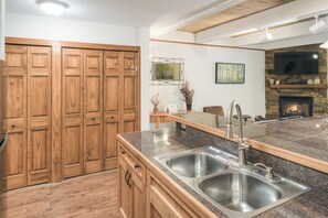 Eine Küche mit Holzausstattung, einer Granit Arbeitsplatte, Edelstahlspülen, einem Kamin und einem Flachbildfernseher.