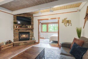 Ein Wohnzimmer mit Kamin aus Stein, einem Flachbildfernseher, einer Holzbalkendecke und einem großen Fenster.