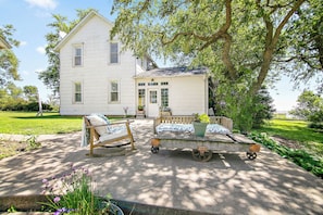 A two-story house with a porch, a small garden, and outdoor furniture.