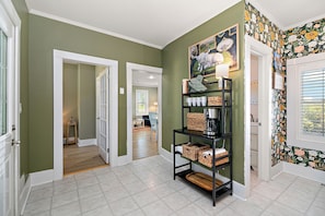 A hallway with green walls, a black shelf with baskets, and a door leading to a room.