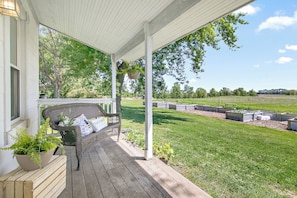 A porch with a wicker chair and potted plants, overlooking a grassy area with raised garden beds.