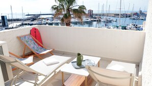 Uma varanda com mesa, cadeiras, uma prancha de surf vermelha e vista para uma marina com barcos.