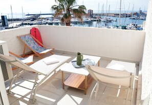 A balcony with a table, chairs, a red surfboard, and a view of a marina with boats.