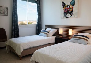 A hotel room with two beds, a window with curtains, a nightstand with lamps, and a painting on the wall.