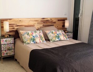 A bedroom with a wooden headboard, two nightstands with floral night lamps, a bed with a black bedspread, and a nightstand with a floral drawer unit.