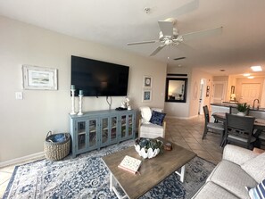 Ein Wohnzimmer mit Fernseher, Deckenventilator, Essbereich und Küche.