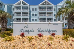 Ein mehrstöckiges Hotel mit Balkonen, einem Schild mit der Aufschrift 'The Grande Caribbean' und einem Kiesgarten mit tropischen Pflanzen.