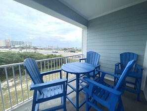 Ein Balkon mit blauen Adirondack-Stühlen und einem Tisch, mit Blick auf eine Straße und Gebäude.