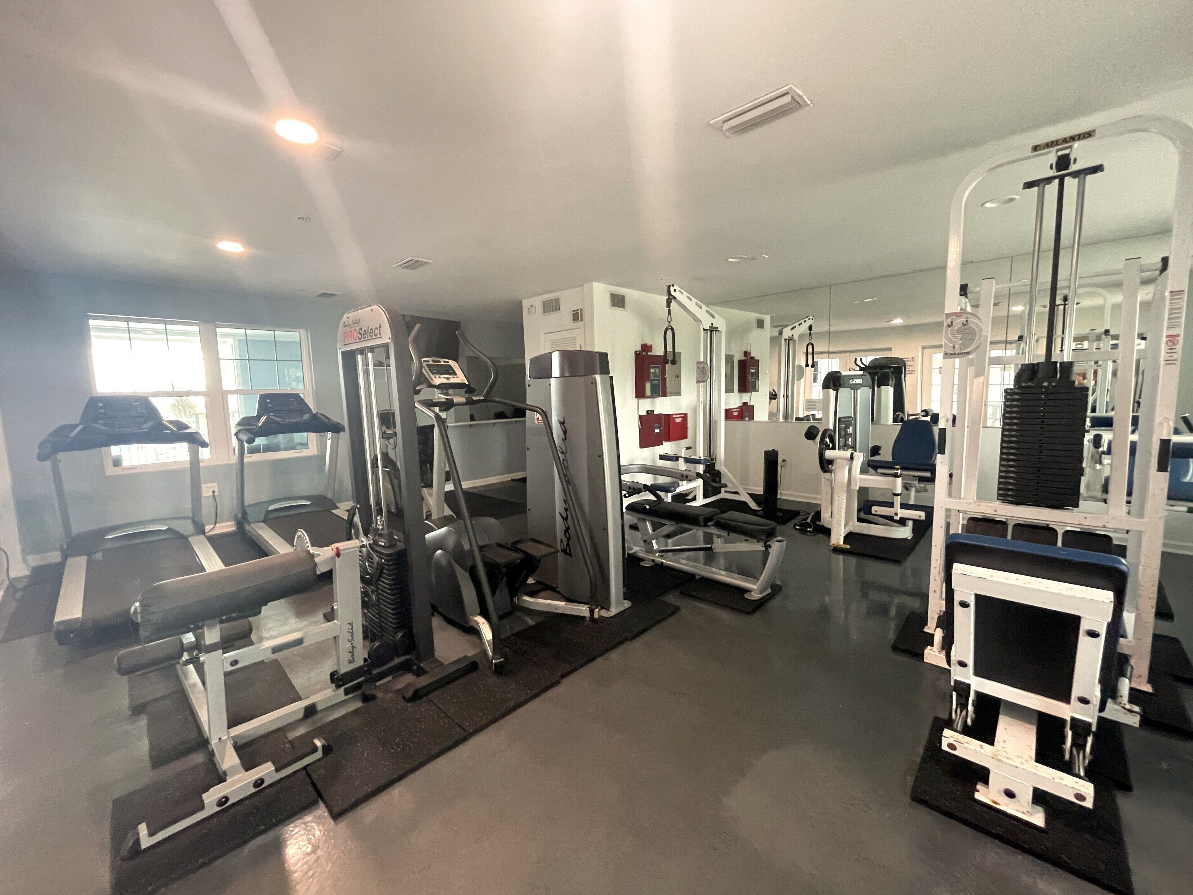 Un gimnasio con cintas de correr, máquinas de pesas y un espejo grande.