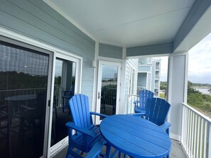 Ein Balkon mit blauen Adirondack-Stühlen und einem Tisch, mit Blick auf ein Gewässer und Gebäude.