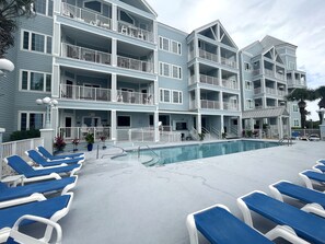 Ein mehrstöckiges Hotel mit Balkonen, einem Pool und Liegestühlen.