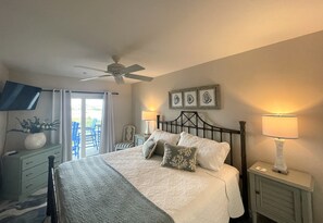 Une chambre à coucher comprenant un lit, des lampes de chevet, un ventilateur de plafond, une table de chevet, une commode et une fenêtre avec des rideaux.