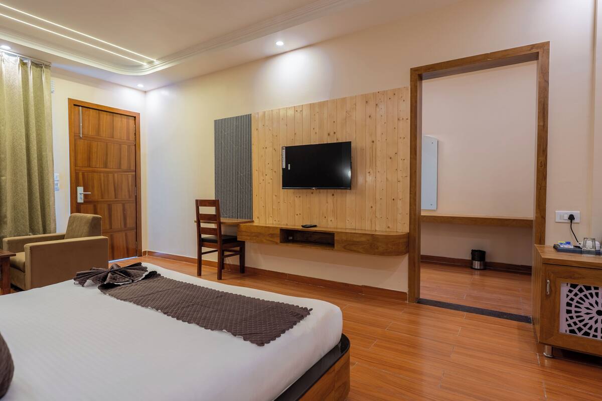 Habitación de hotel con cama, televisor montado en una pared de paneles de madera, escritorio con silla y armario.