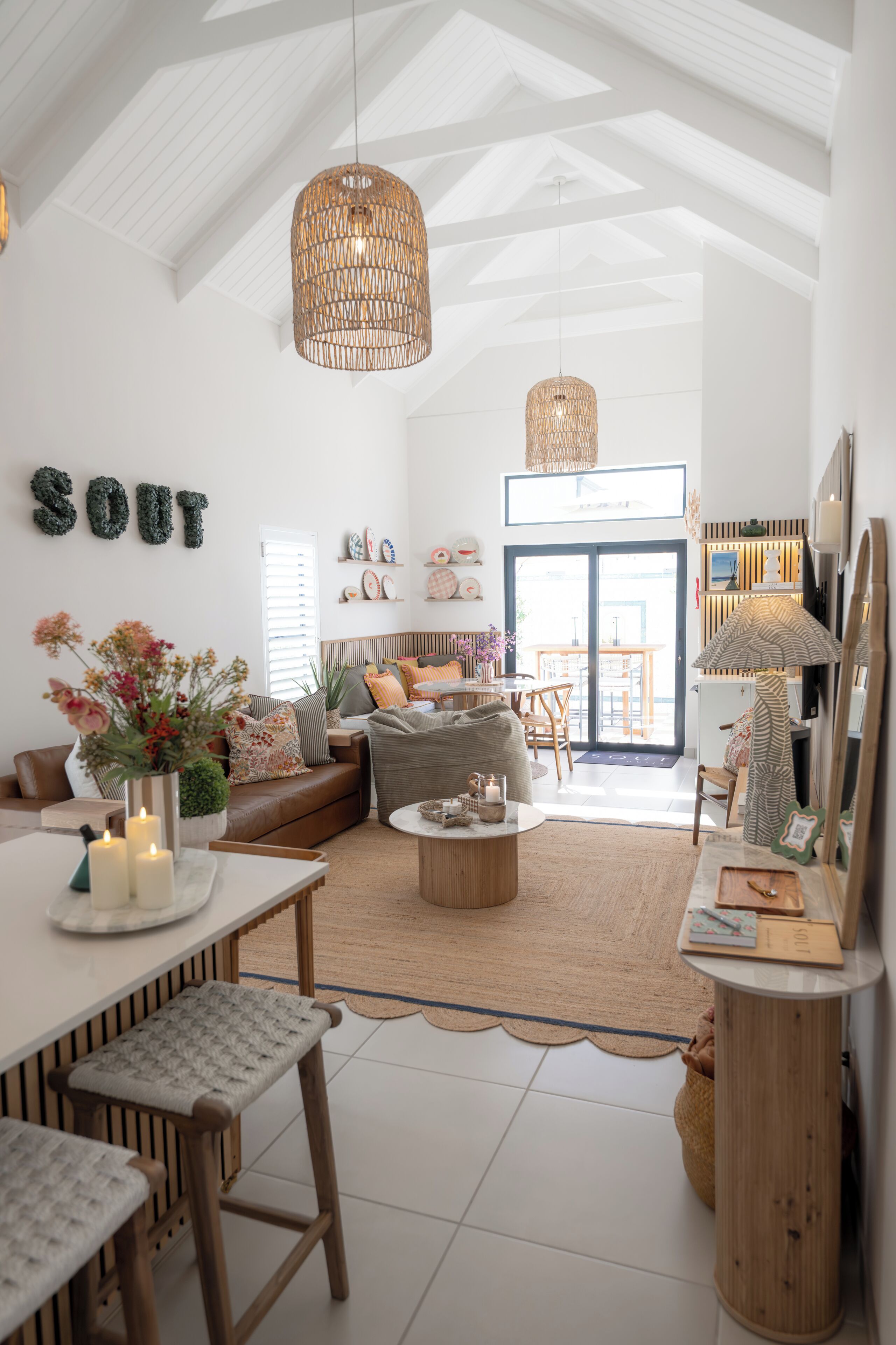 A spacious living room with a high ceiling, a dining area with a table and chairs, a sofa, and a large window.