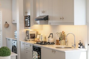 A modern kitchen with white cabinets, a built-in oven, a stove, a coffee maker, and a sink. - Sout Huijs Langebaan - A little slice of West Coast Heaven with Hot Tub (Langebaan)