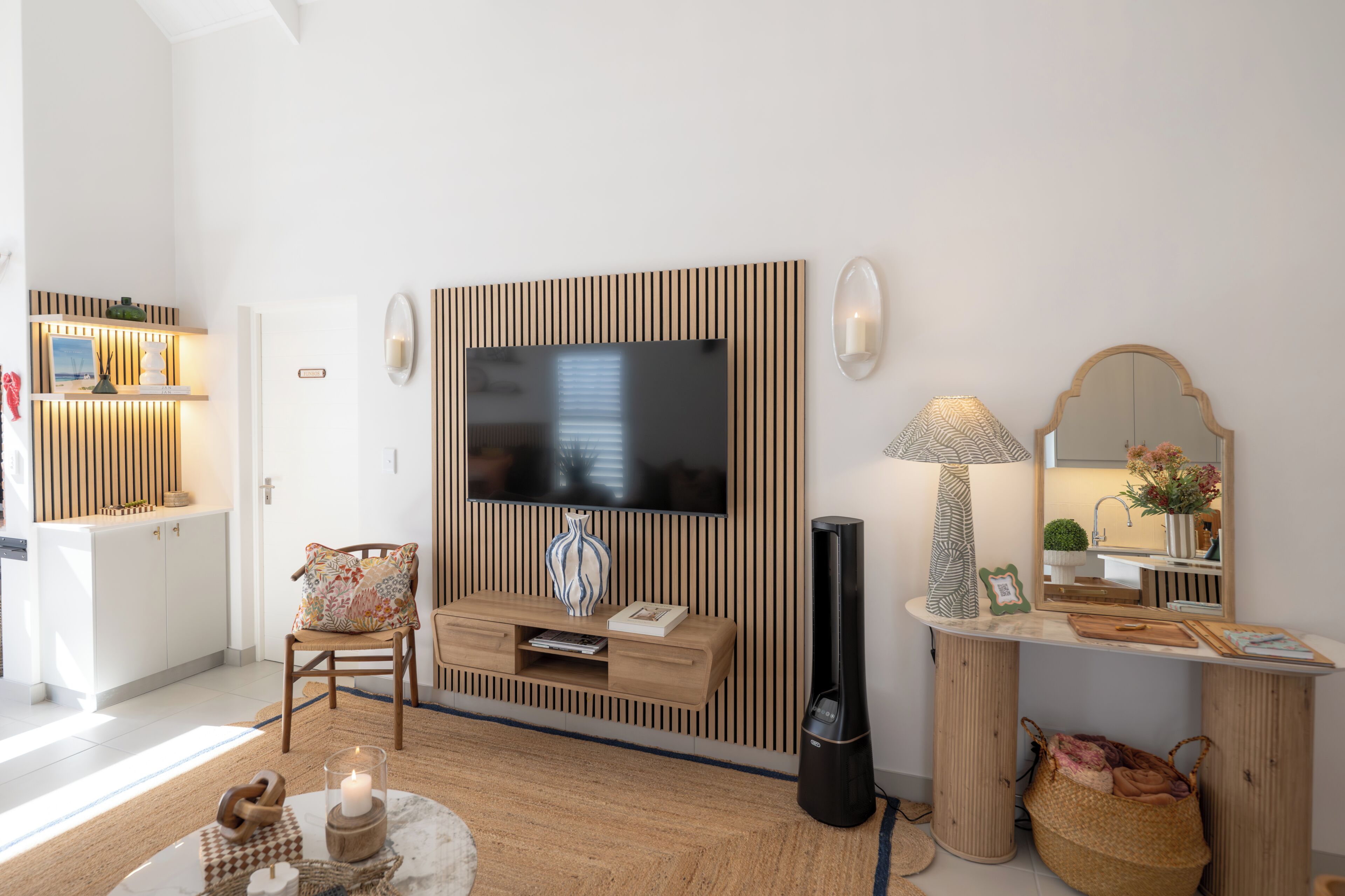 Un salon moderne avec un téléviseur, un mur recouvert de panneaux en bois, une lampe, un miroir et une petite table agrémentée d’objets décoratifs.