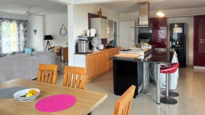 Cozinha moderna com ilha central, sala de jantar com mesa de madeira e sala de estar com sofá.