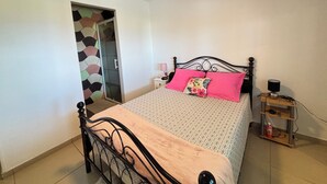 Quarto com cama, mesa de cabeceira, abajur, guarda-roupa e ventoinha no teto.