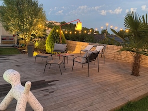 Une terrasse en bois, dotée de mobilier d’extérieur, de guirlandes lumineuses et d’un lampadaire décoratif.