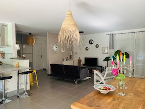Un salon moderne avec un canapé noir, une table à manger en bois et un coin cuisine doté d’un tabouret de bar.