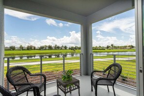 Un balcon avec deux fauteuils en osier et une petite table, donnant sur un plan d’eau et des champs verdoyants.