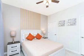 Une chambre à coucher comprenant un lit, deux tables de chevet, un ventilateur de plafond, une porte et un mur à rayures verticales.