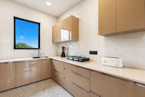 A modern kitchen with a window, a stove, a toaster, and cabinets. - ELIVAAS Panchvati Veloraa 6BHK (Solan)