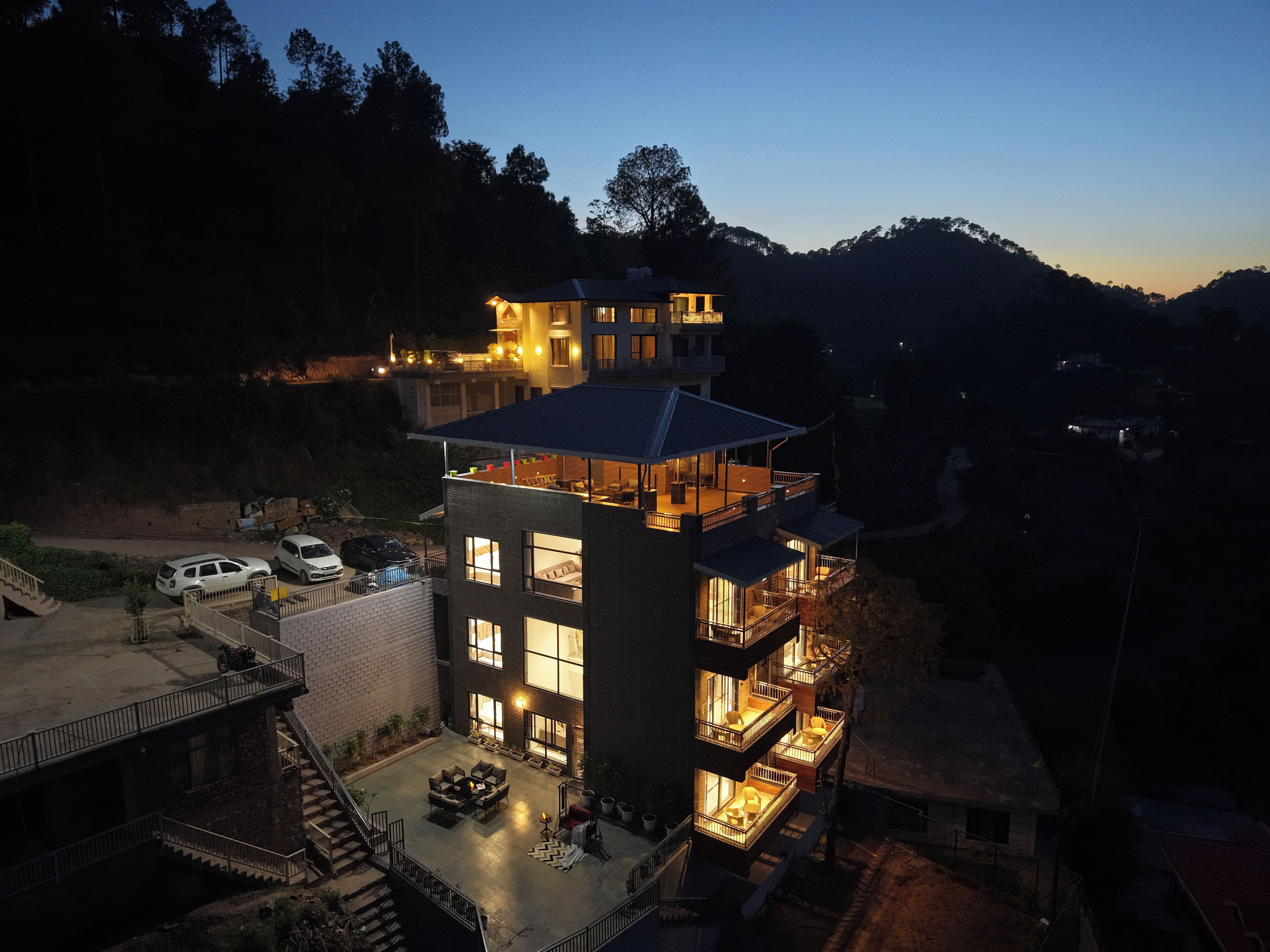 Un edificio de varios pisos con balcones, un patio amoblado y vistas del paisaje circundante.
