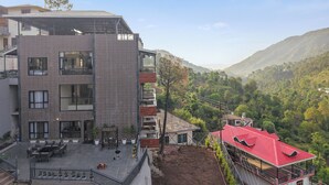 Un edificio a più piani con una terrazza sul tetto, un balcone e vista su un paesaggio collinare.